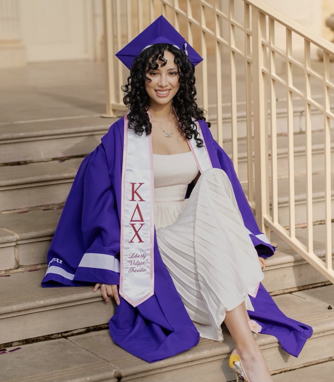 Liberty Trevino sitting on stairs wearing purple cap and gown
